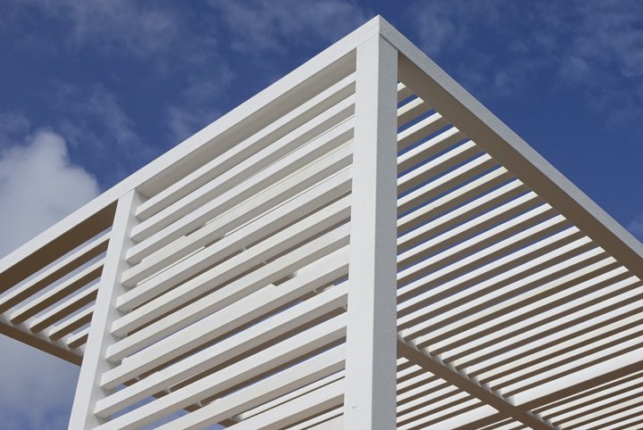 Looking up at a white slatted pergola roof against a blue sky