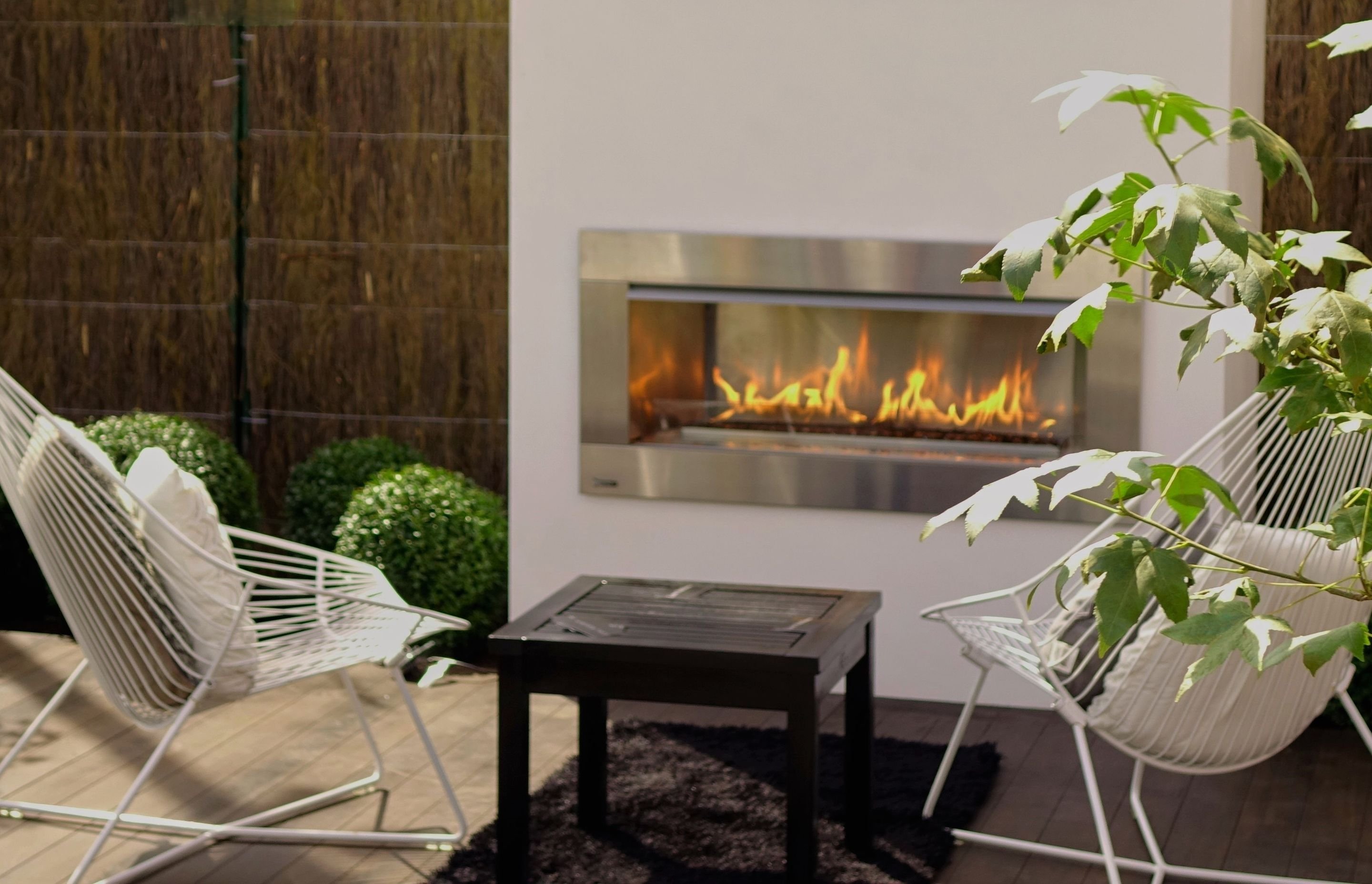Courtyard seating area with white wire chairs facing a linear gas fireplace set into a white wall
