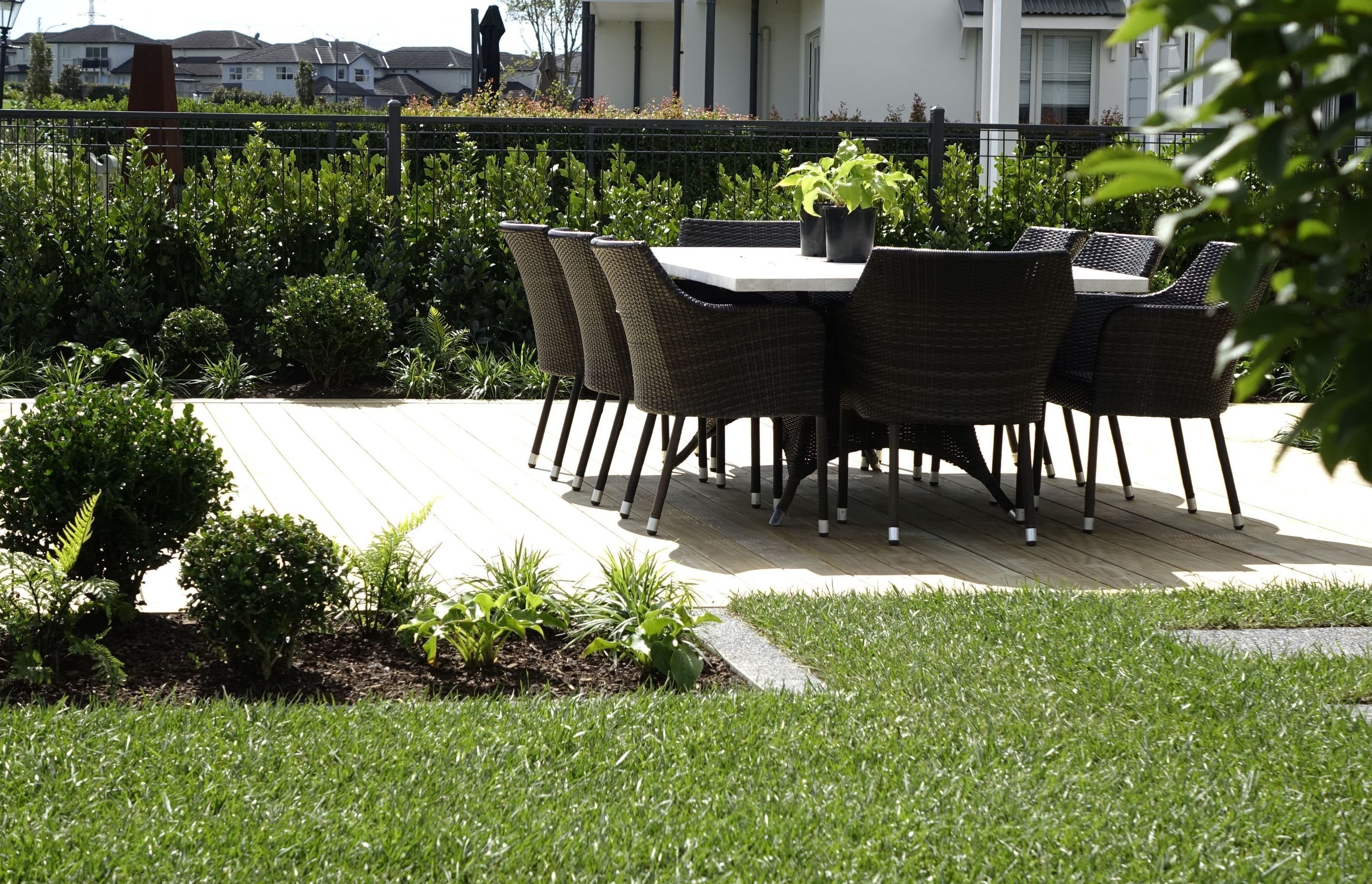 Timber deck with a wicker dining setting, edged by clipped hedging and layered garden beds