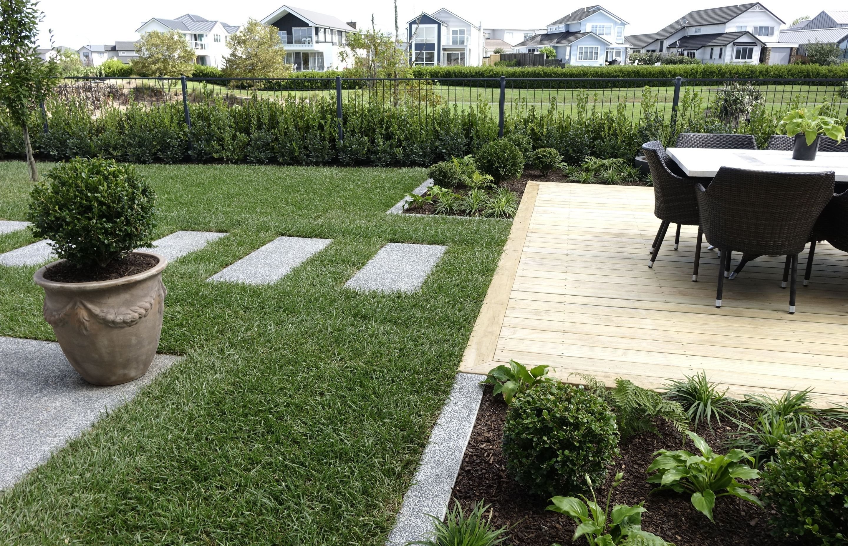 Lawn with granite stepping stones leading to a timber deck set with outdoor dining chairs